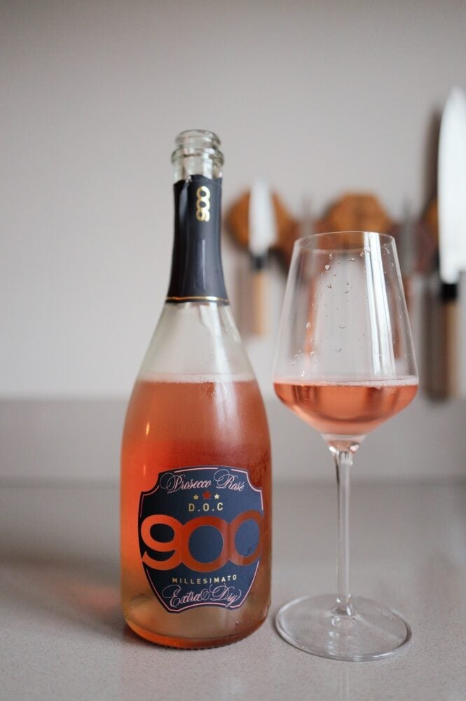 900 Prosecco DOC Rosé bottle and a glass of salmon-pink sparkling wine on a counter