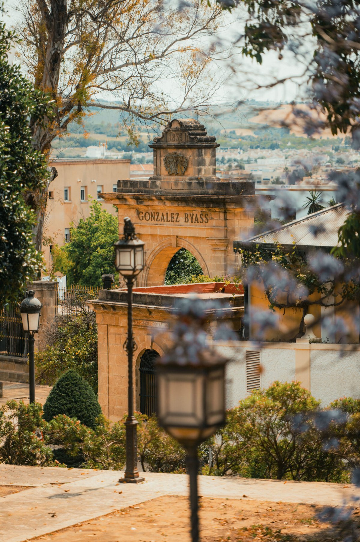 Stone archway of the González Byass bodega framed by trees and a vintage street lamp