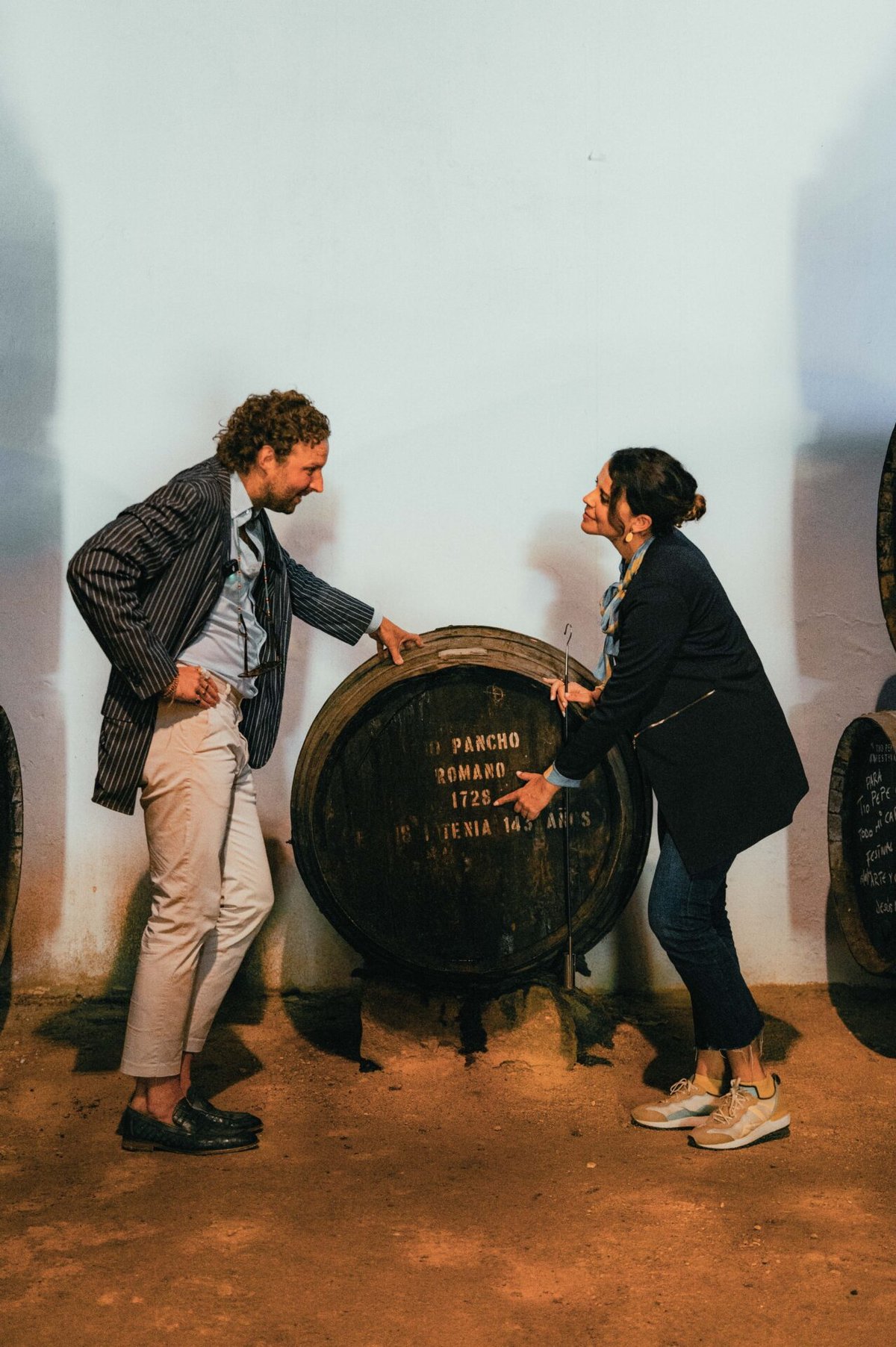 A glass of dark amber sherry held in the foreground, a smiling woman blurred behind it