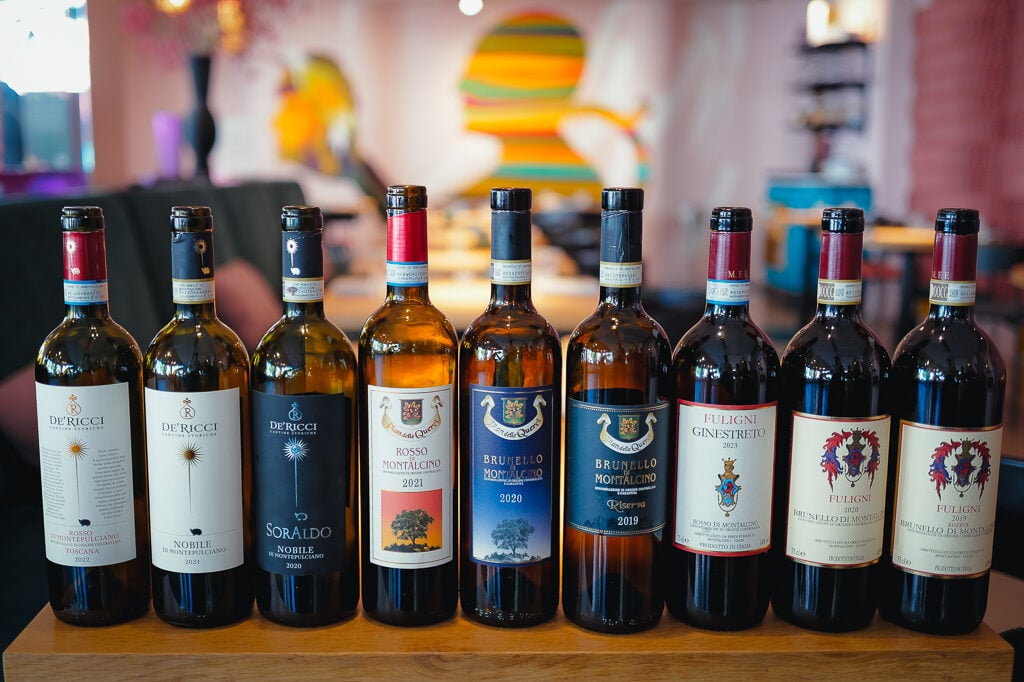 A lineup of nine Tuscan wine bottles from De' Ricci, Brunello and Fuligni on a table