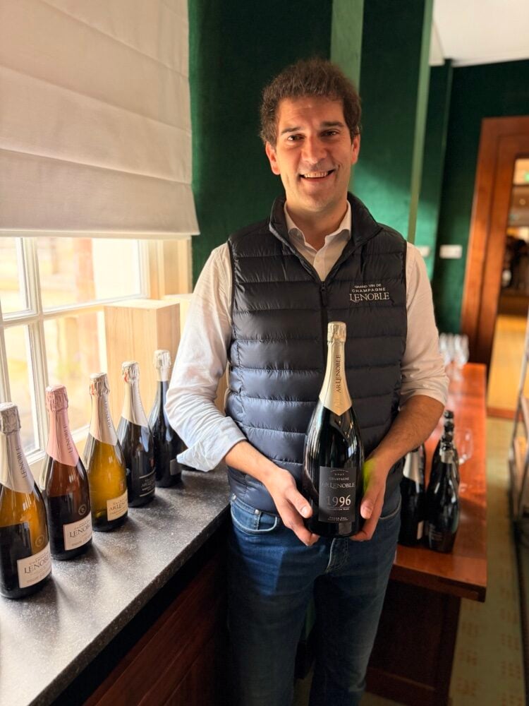A smiling man in an AR Lenoble gilet holds a magnum of 1996 Champagne by a window
