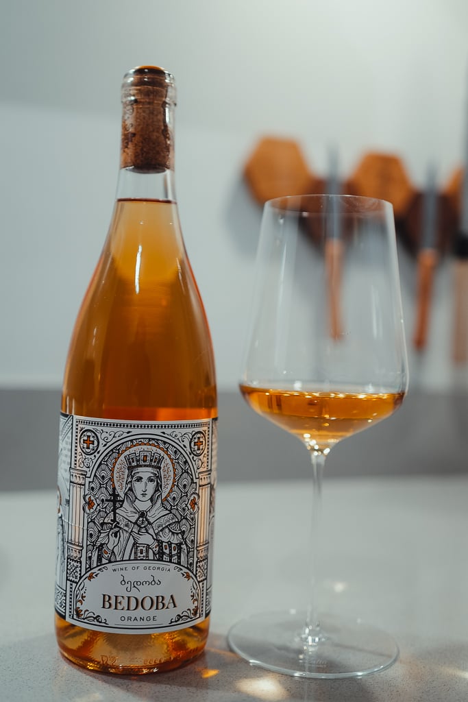 Bedoba Orange bottle with an icon-style saint label beside a glass of amber wine