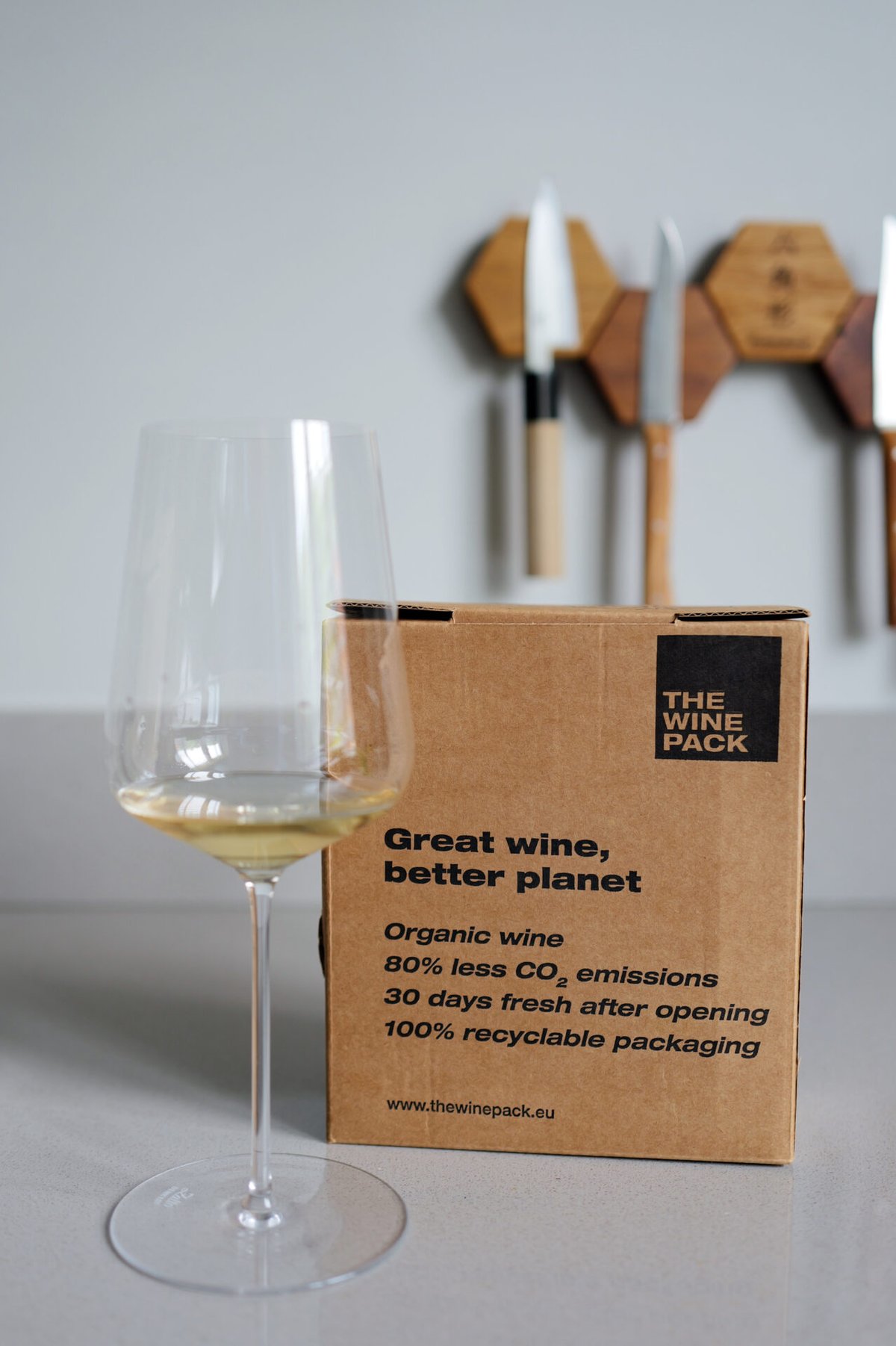 A glass of white wine beside a kraft The Wine Pack box reading Great wine, better planet