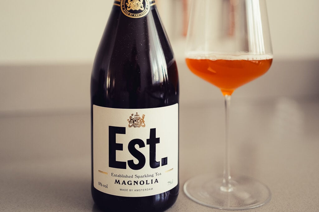 Est. Established Sparkling Tea Magnolia bottle beside a wine glass of amber tea