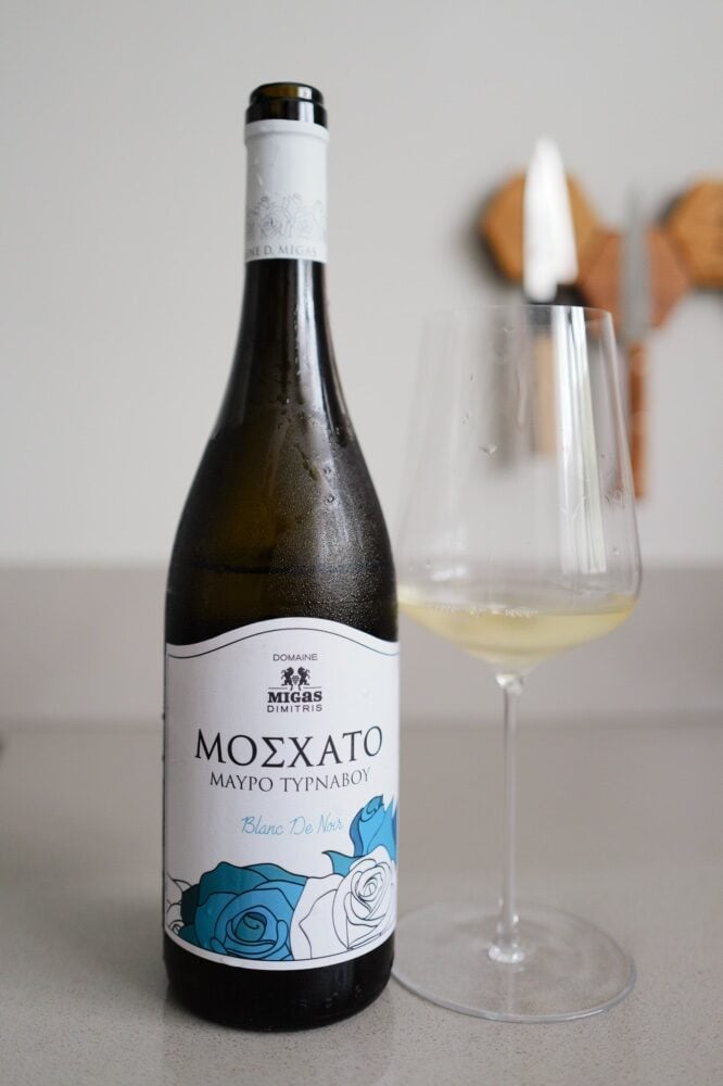 Domaine Migas Moschato Blanc de Noir bottle with blue rose label beside a glass of white wine