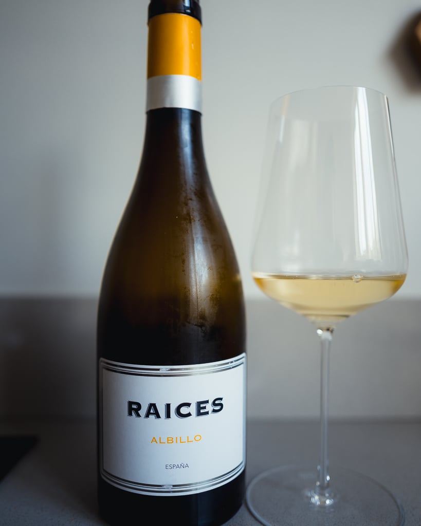 Raices Albillo white wine bottle from Spain next to a glass of pale golden wine