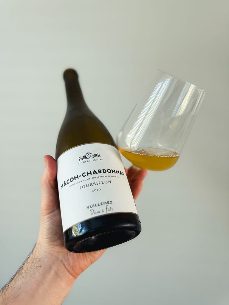 Hand holding a Mâcon-Chardonnay Tourbillon bottle next to a glass of white wine