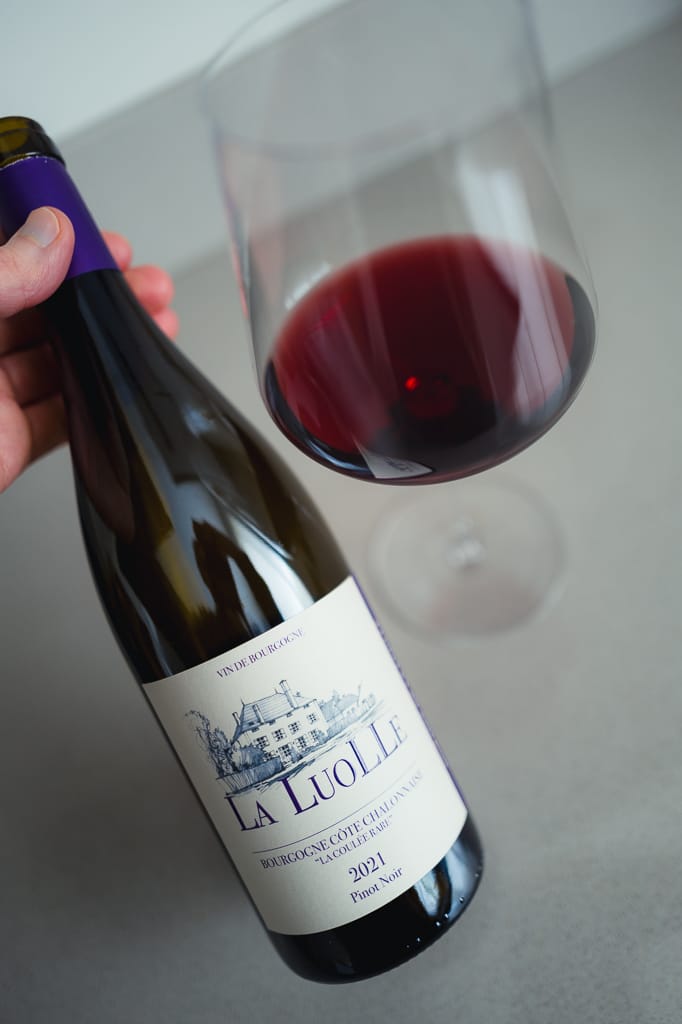 Hand holding the La Luolle Bourgogne Pinot Noir bottle by a glass of red wine