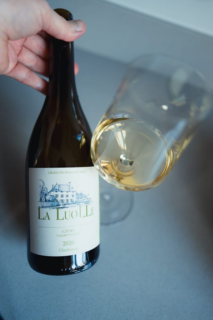 Hand holding the La Luolle Givry Chardonnay bottle above a glass of white wine
