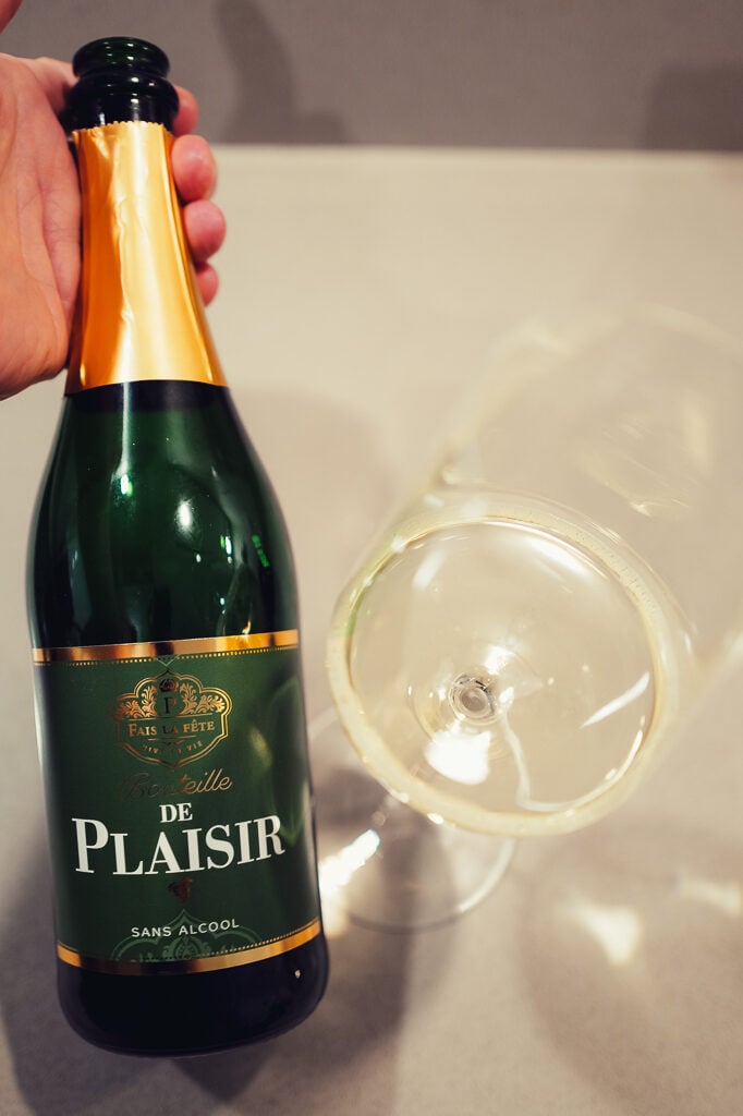 Green Bouteille de Plaisir Sans Alcool bottle with gold foil held beside a glass