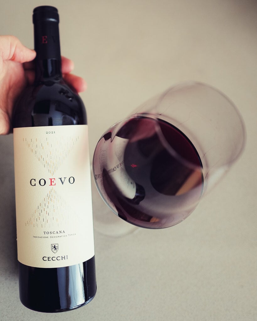 Hand holding the Cecchi Coevo 2021 bottle above a glass of red wine