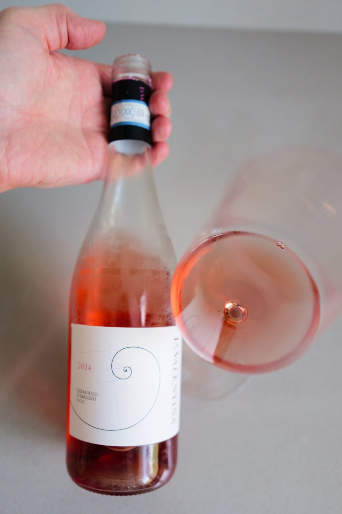 Hand holding the La Valentina Cerasuolo bottle above a glass of bright cherry-pink rosé