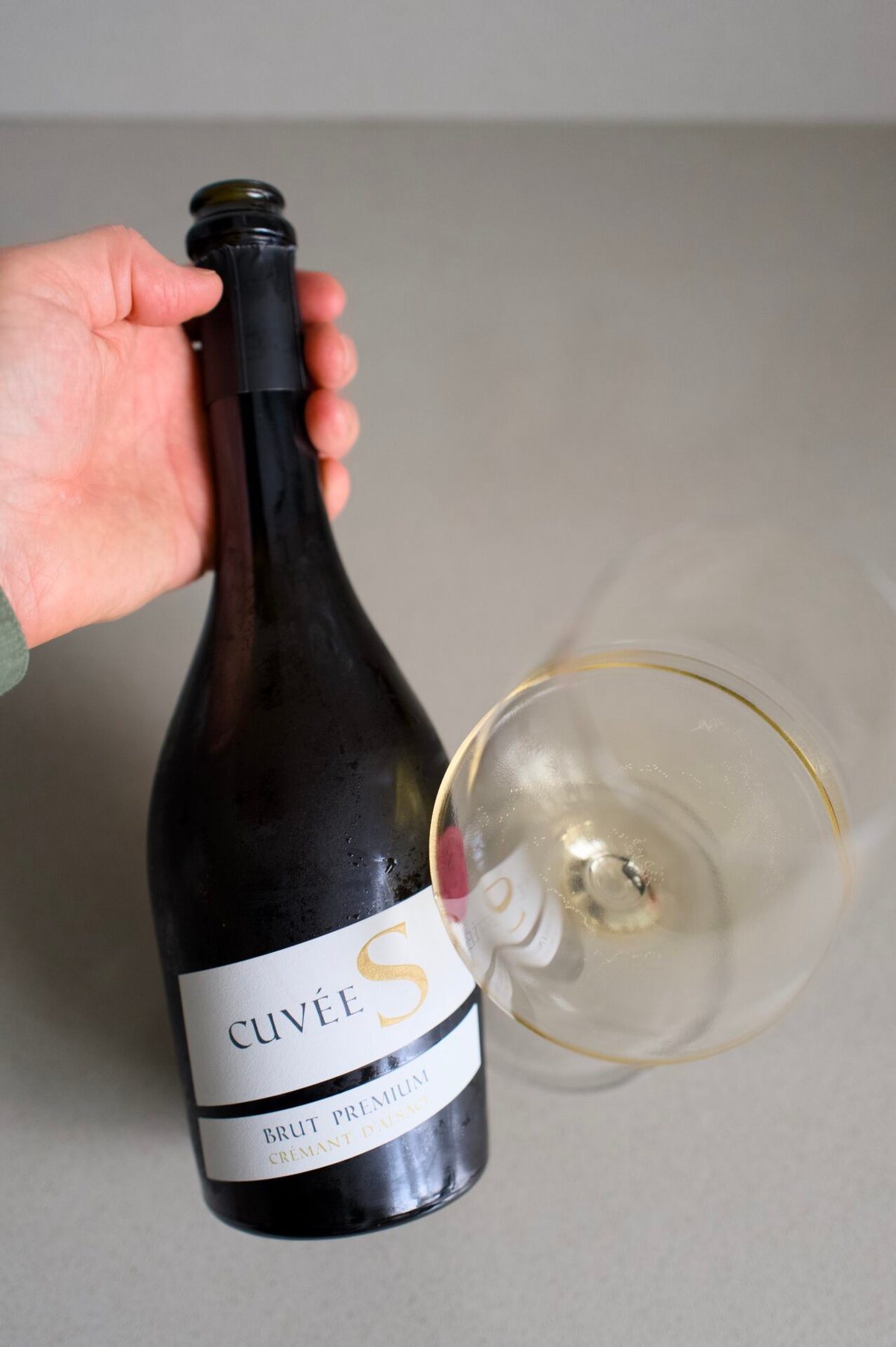 Hand holding the Cuvée S Crémant d'Alsace bottle above a glass of sparkling wine