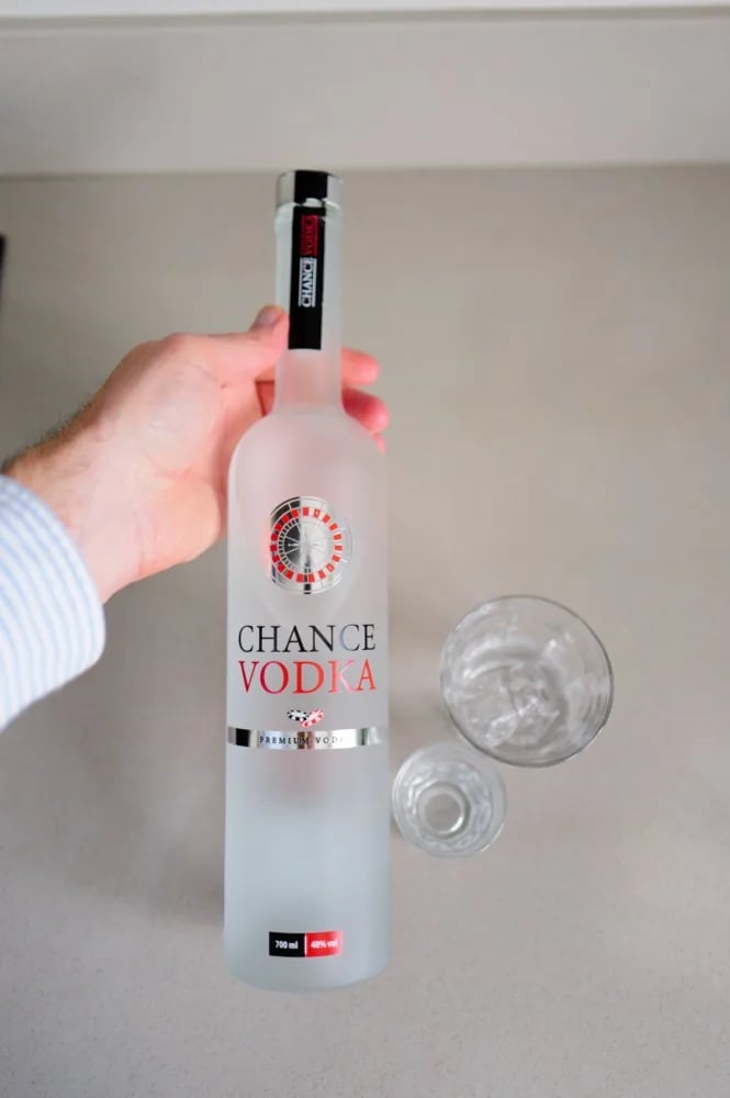 Hand holding the frosted Chance Vodka bottle above the counter, with two glasses beside it