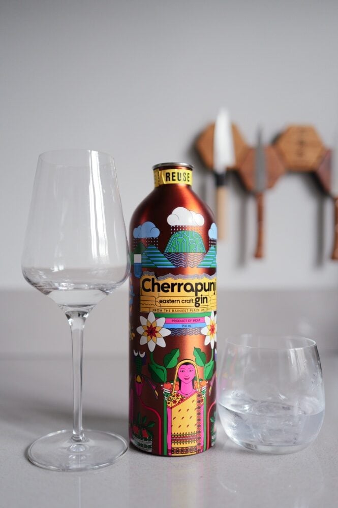 Colourful Cherrapunji craft gin tin bottle between an empty wine glass and a tumbler