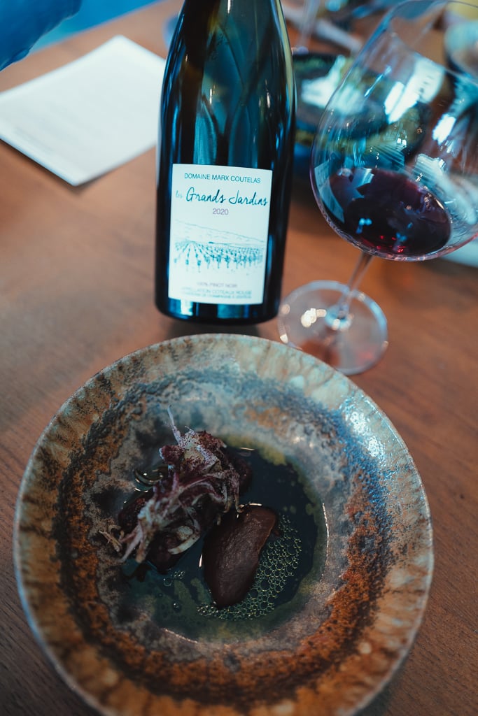 A Marx-Coutelas Grands Jardins red wine bottle and a glass of red beside an earthy course in a bowl