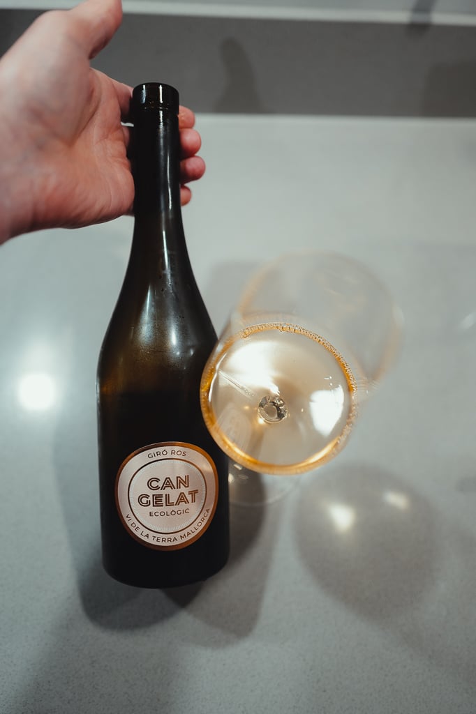 Hand holding the Can Gelat Giró Ros bottle beside a tilted glass of amber orange wine
