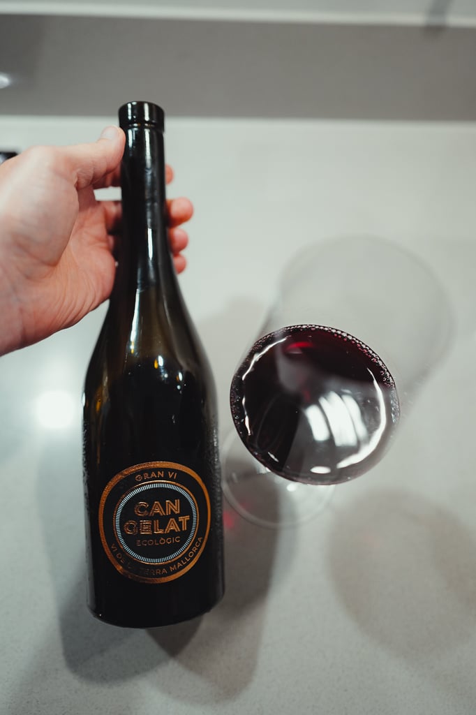 Hand holding the Can Gelat Gran Vi bottle beside a tilted glass of deep red wine