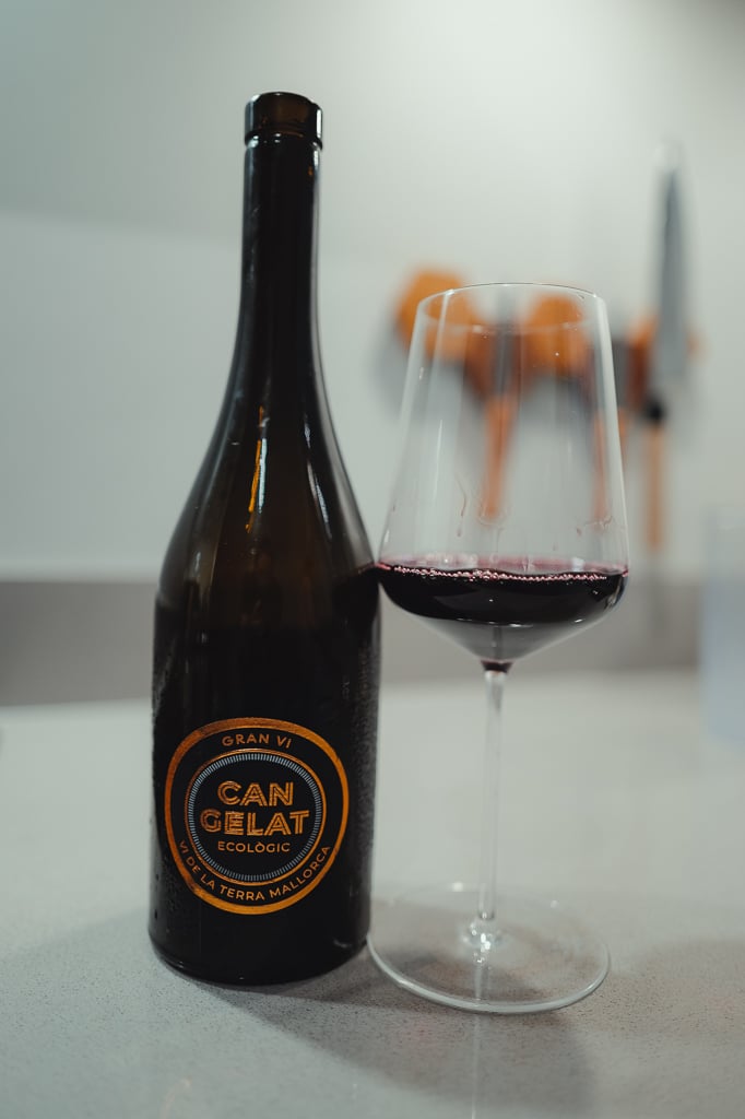 Can Gelat Gran Vi bottle with a dark label beside a glass of deep red wine on a white counter