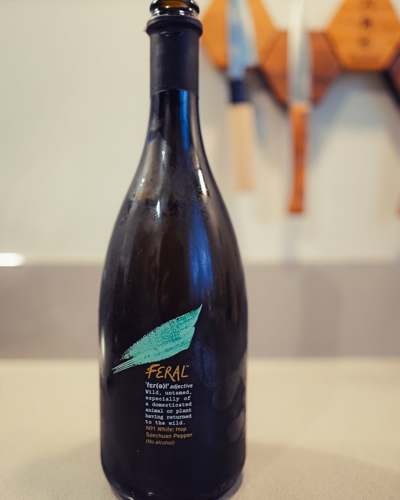 Dark Feral No1 White bottle with a teal brushstroke label and dictionary definition on a kitchen counter