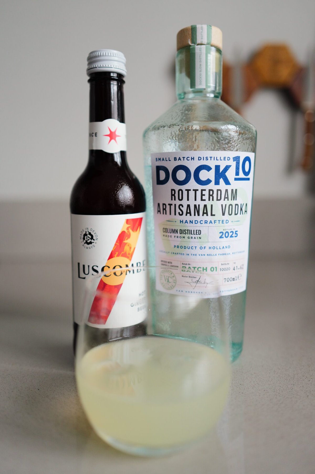 DOCK10 Rotterdam Vodka beside a Luscombe ginger bottle and a cloudy cocktail in a coupe