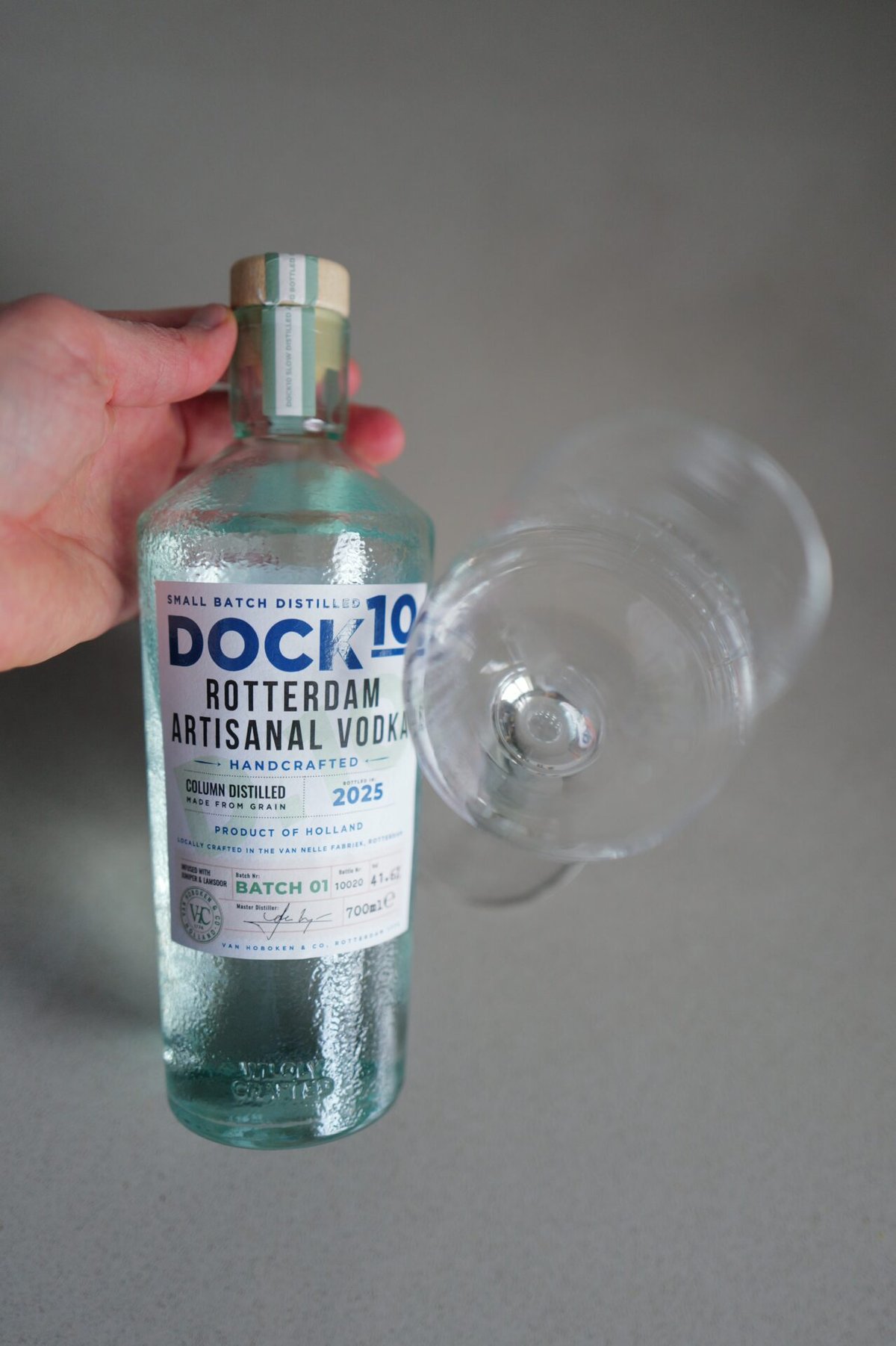 Hand holding the DOCK10 Rotterdam Vodka bottle beside a tilted empty wine glass