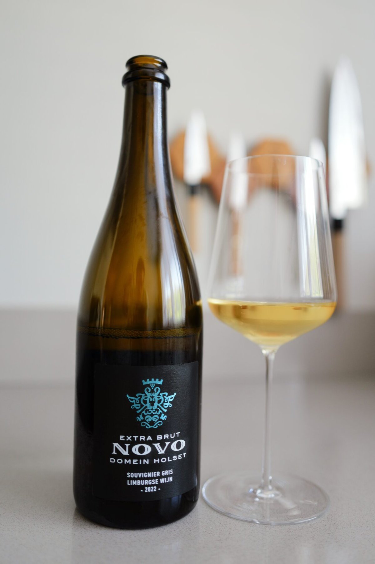 Domein Holset Novo bottle with black Extra Brut label standing beside a glass of golden sparkling wine