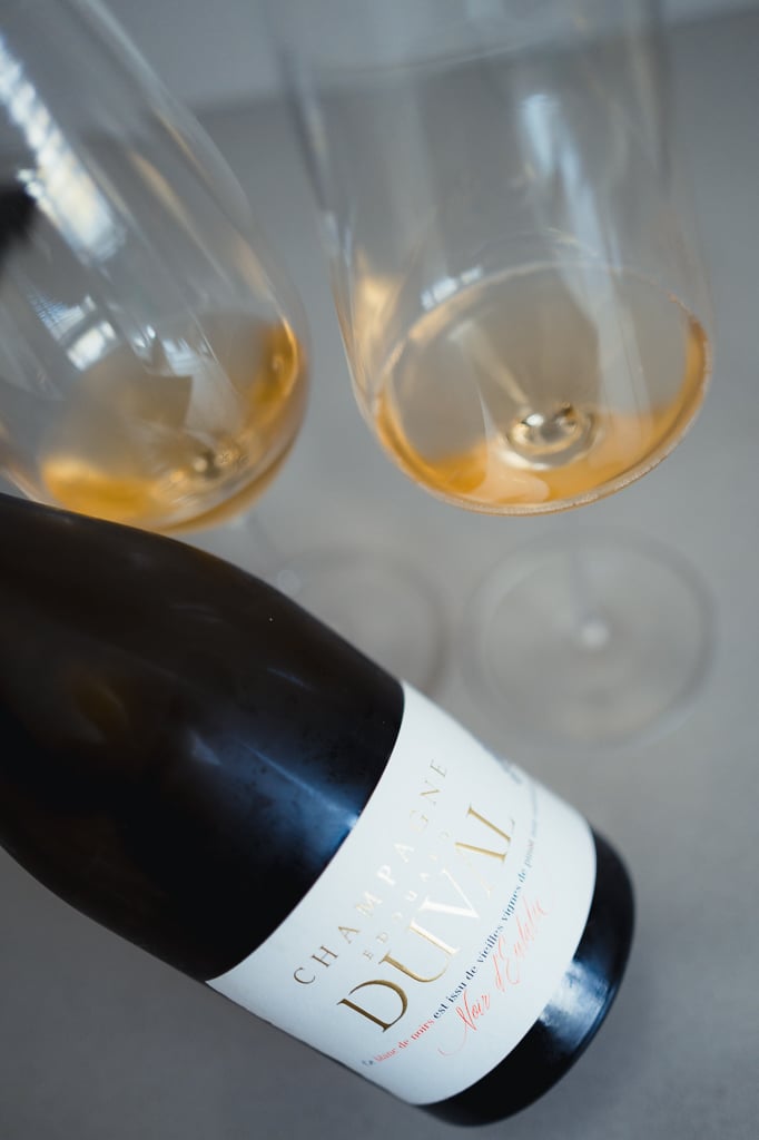 Two glasses of amber champagne seen from above with the Noir d'Eulalie bottle lying alongside