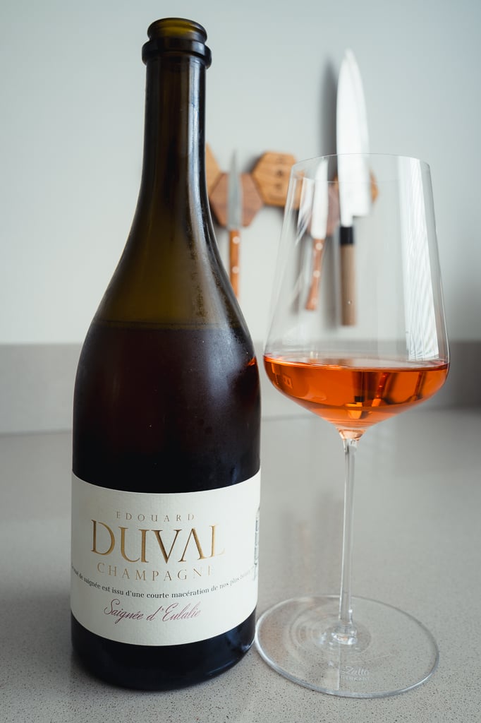 Edouard Duval Saignée d'Eulalie bottle beside a glass of salmon-pink rosé champagne on a counter