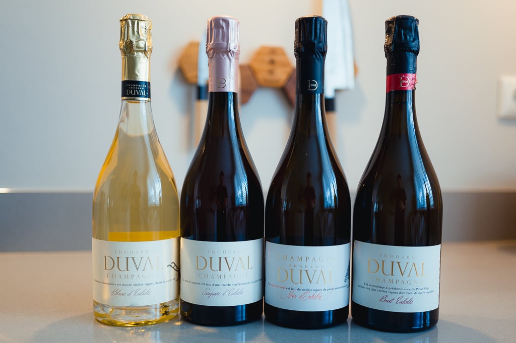Four Edouard Duval Champagne bottles standing in a row, two with gold and pink foils and two with dark caps