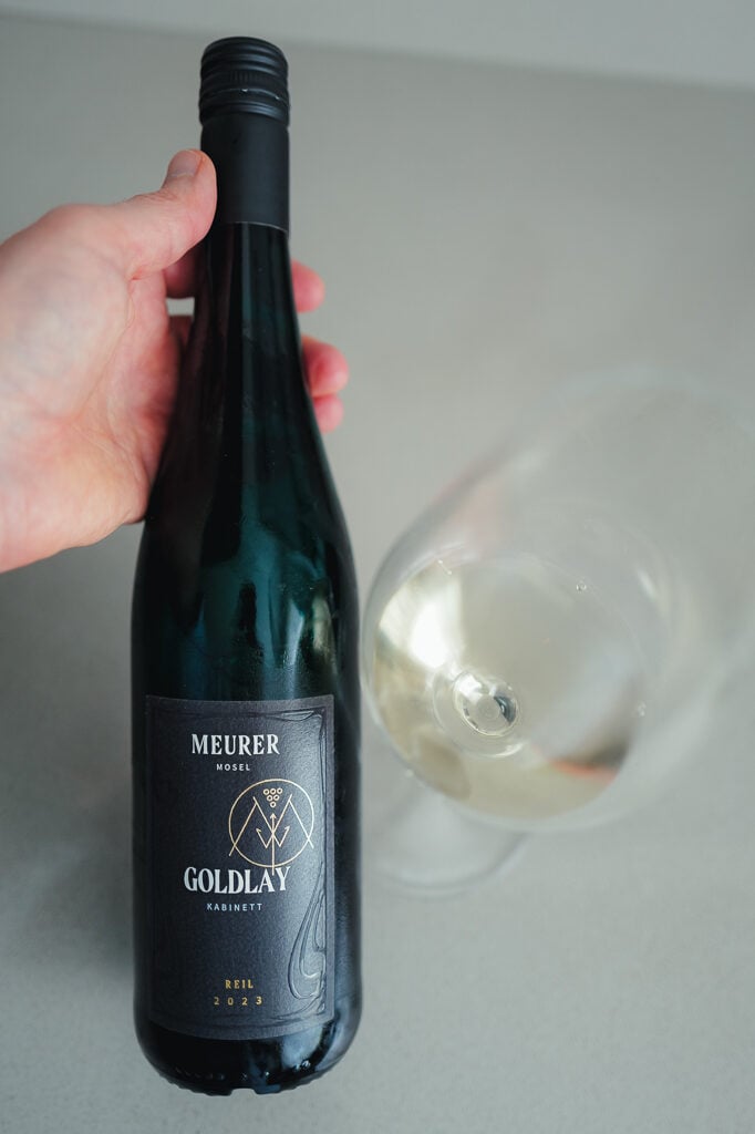 Hand holding the Meurer Goldlay Kabinett bottle beside a tilted glass of white wine