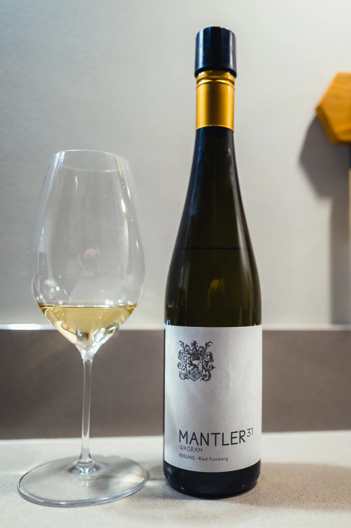Mantler 31 Riesling Ried Fumberg bottle with gold foil beside a glass of white wine