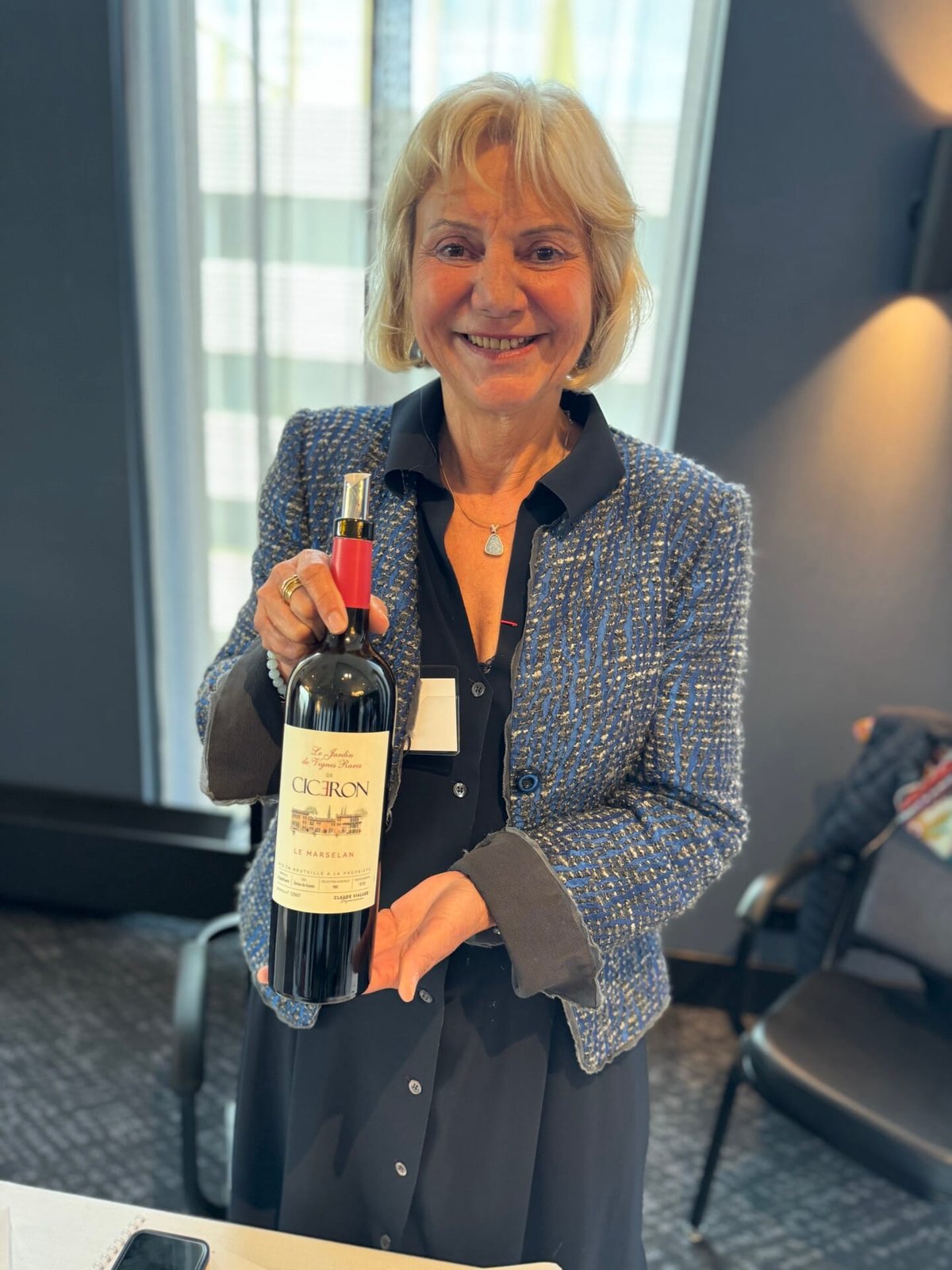 Smiling woman in a blue tweed jacket holding a bottle of Cicéron Le Marselan red wine