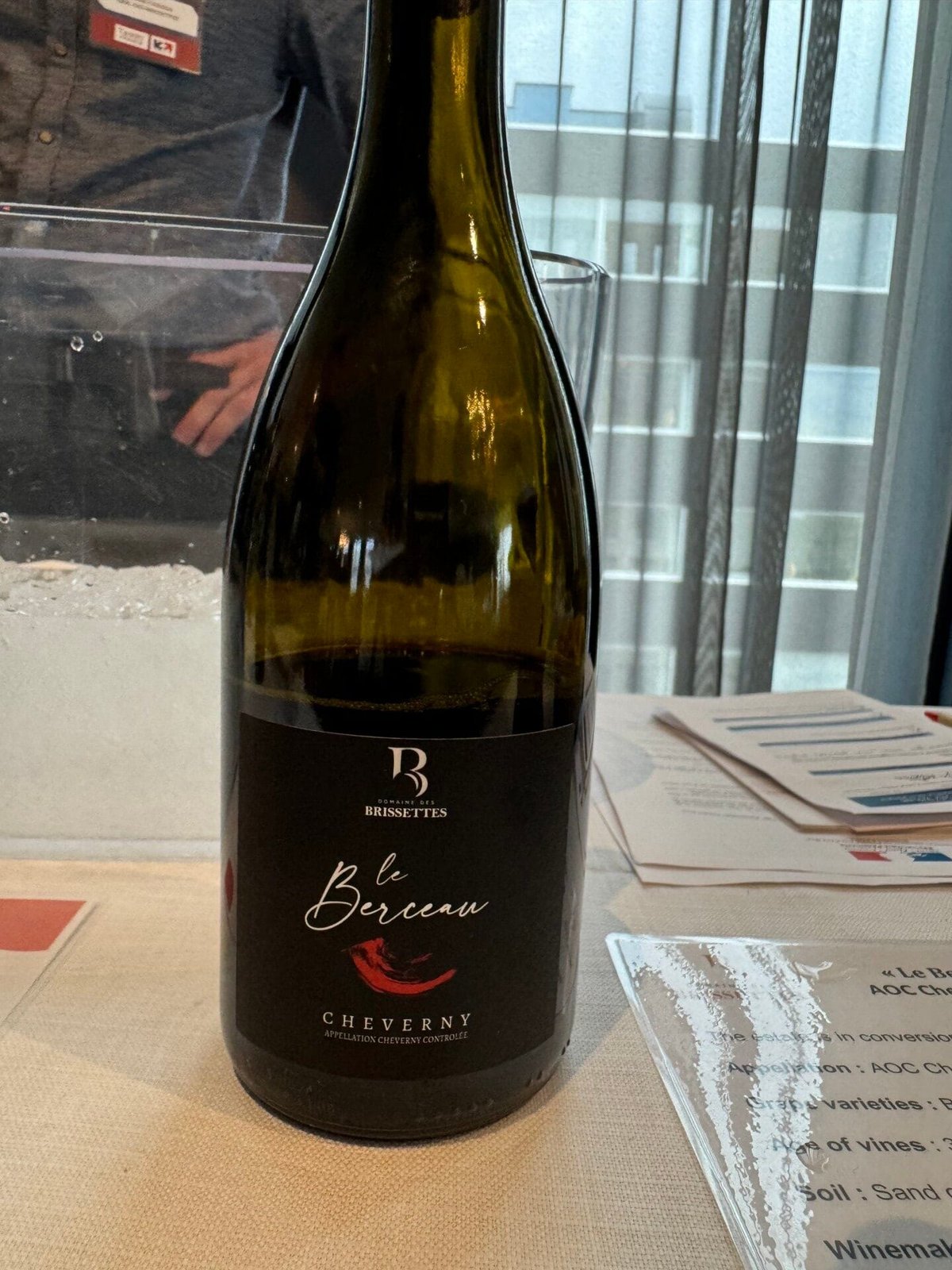 Hand holding a dark bottle of Domaine des Brissettes Le Berceau Cheverny at the tasting table