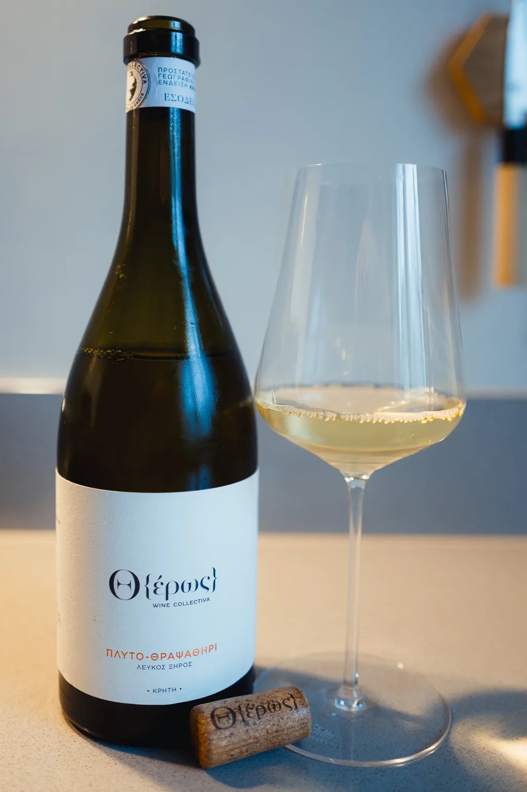 Bottle of Theros Plyto-Thrapsathiri with a glass of white wine and a branded cork