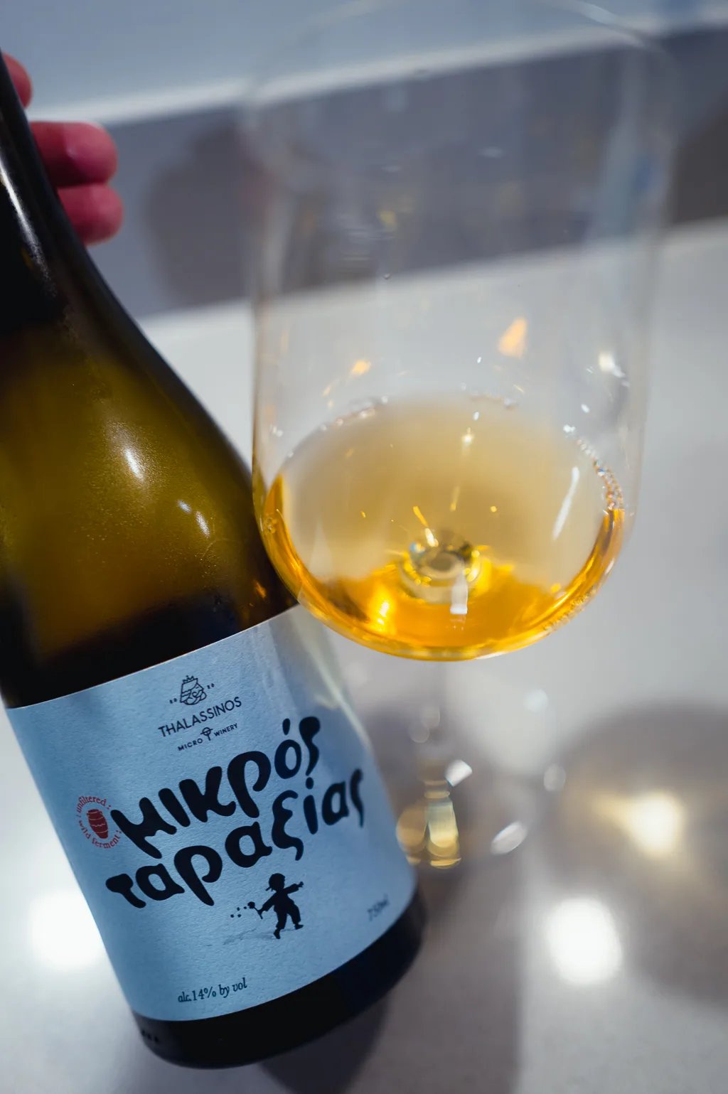 Reclining Thalassinos Mikrós Taraxías bottle beside a tilted glass of amber wine