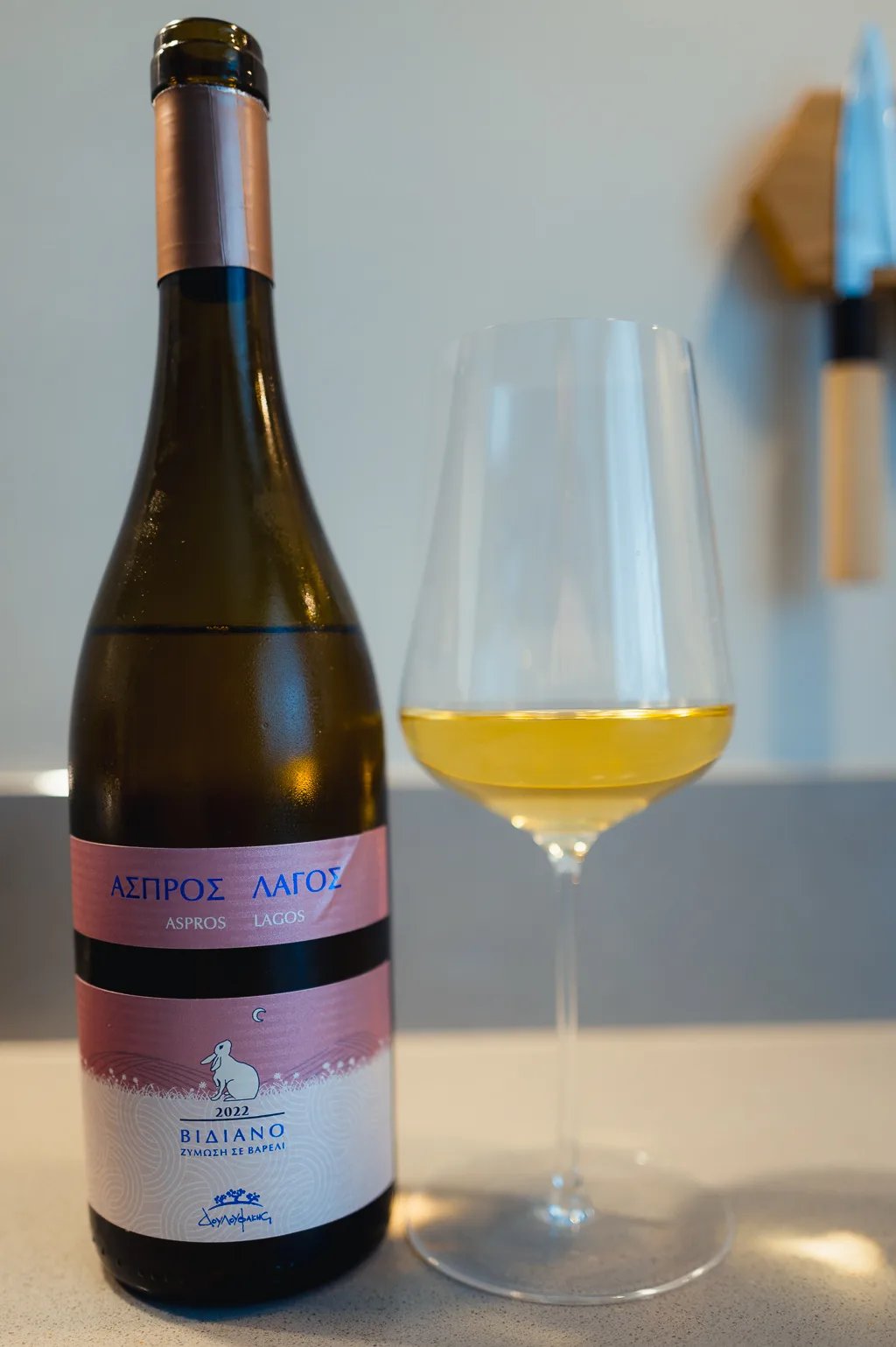 Bottle of Douloufakis Aspros Lagos Vidiano 2022 next to a glass of golden white wine