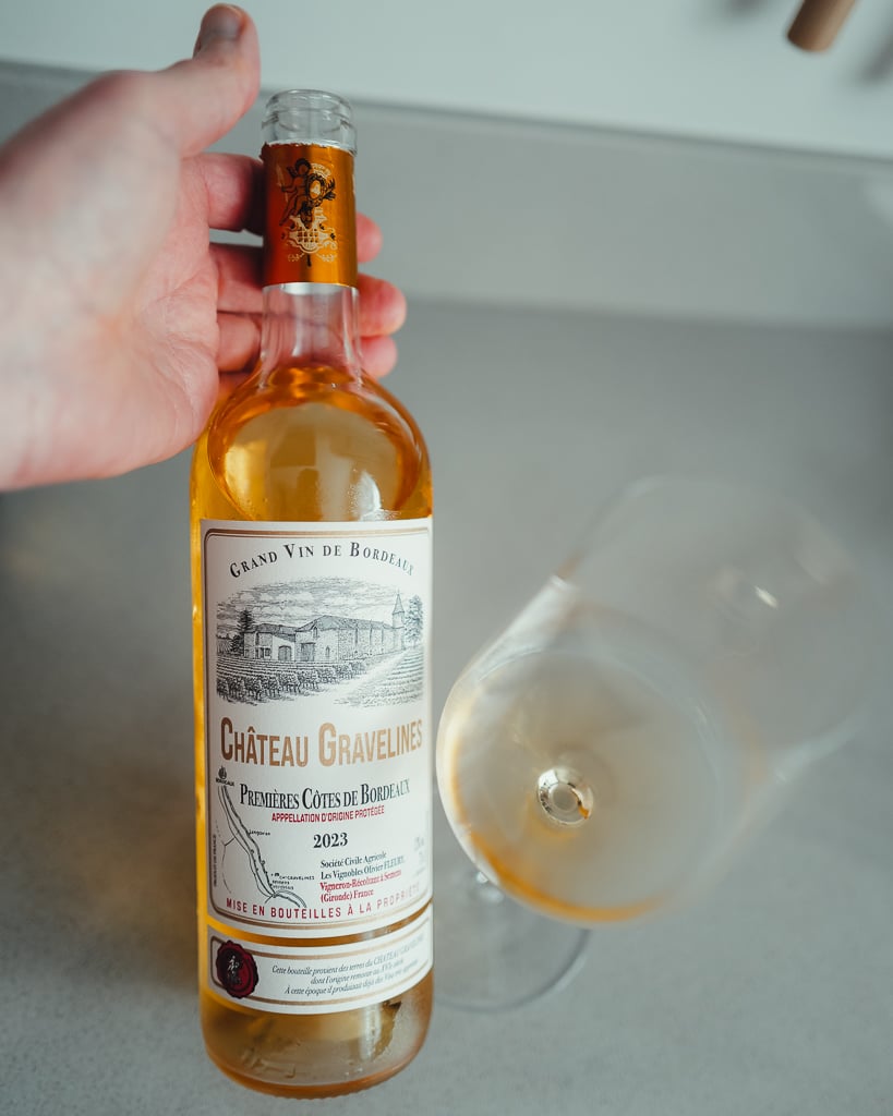 Hand holding a bottle of Château Gravelines 2023 sweet white beside a tilted glass