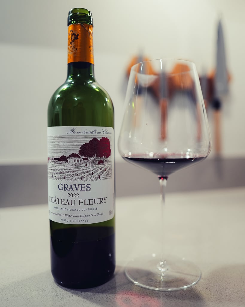 Château Fleury Graves red bottle with illustrated vineyard label beside a glass of red wine