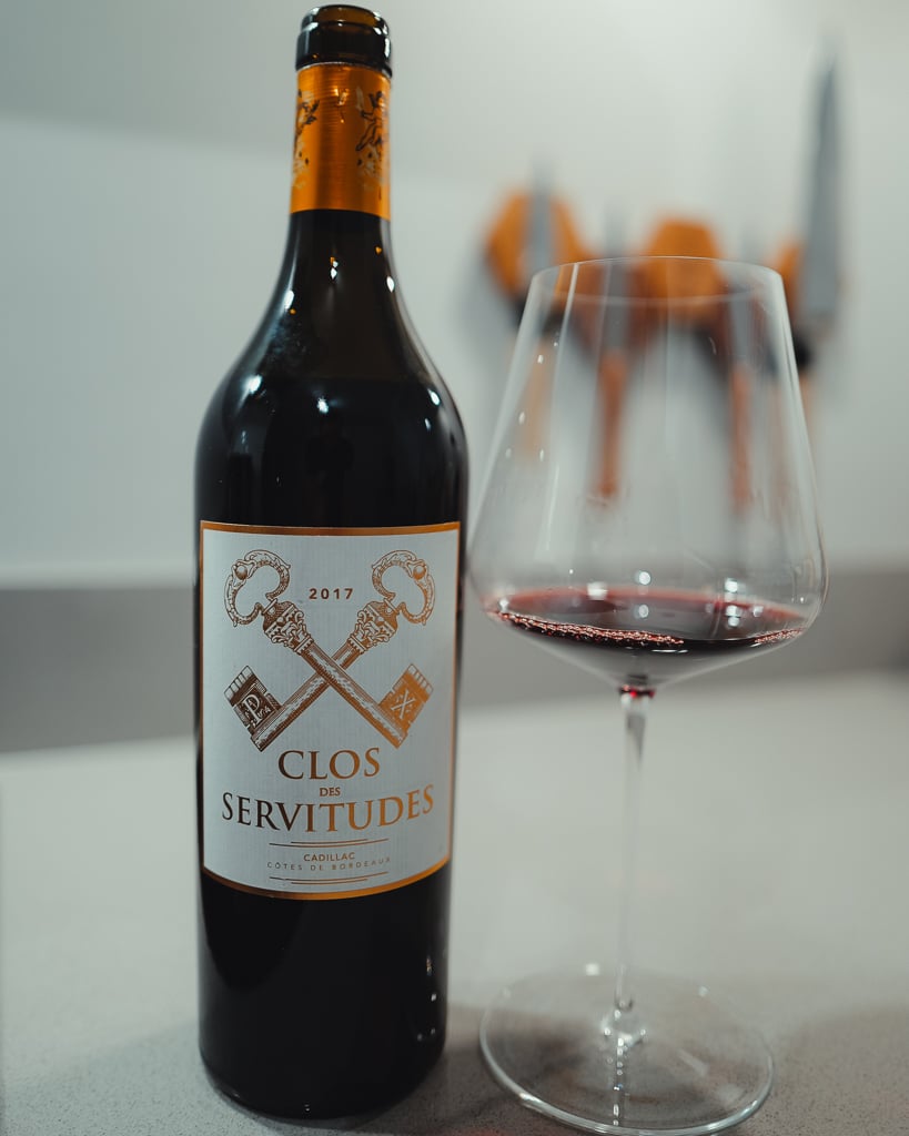 Standing bottle of Clos des Servitudes 2017 Cadillac red next to a glass of red wine