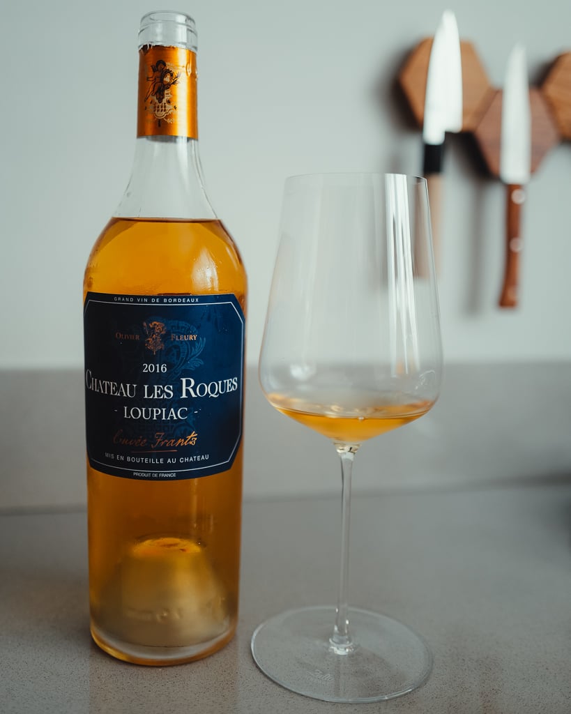 Standing bottle of Château Gravelines 2023 sweet white beside a glass of amber wine