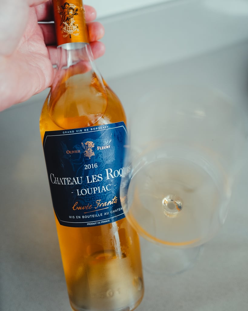 Hand holding a bottle of Château Les Roques 2016 Loupiac Cuvée Frantz with a blue label