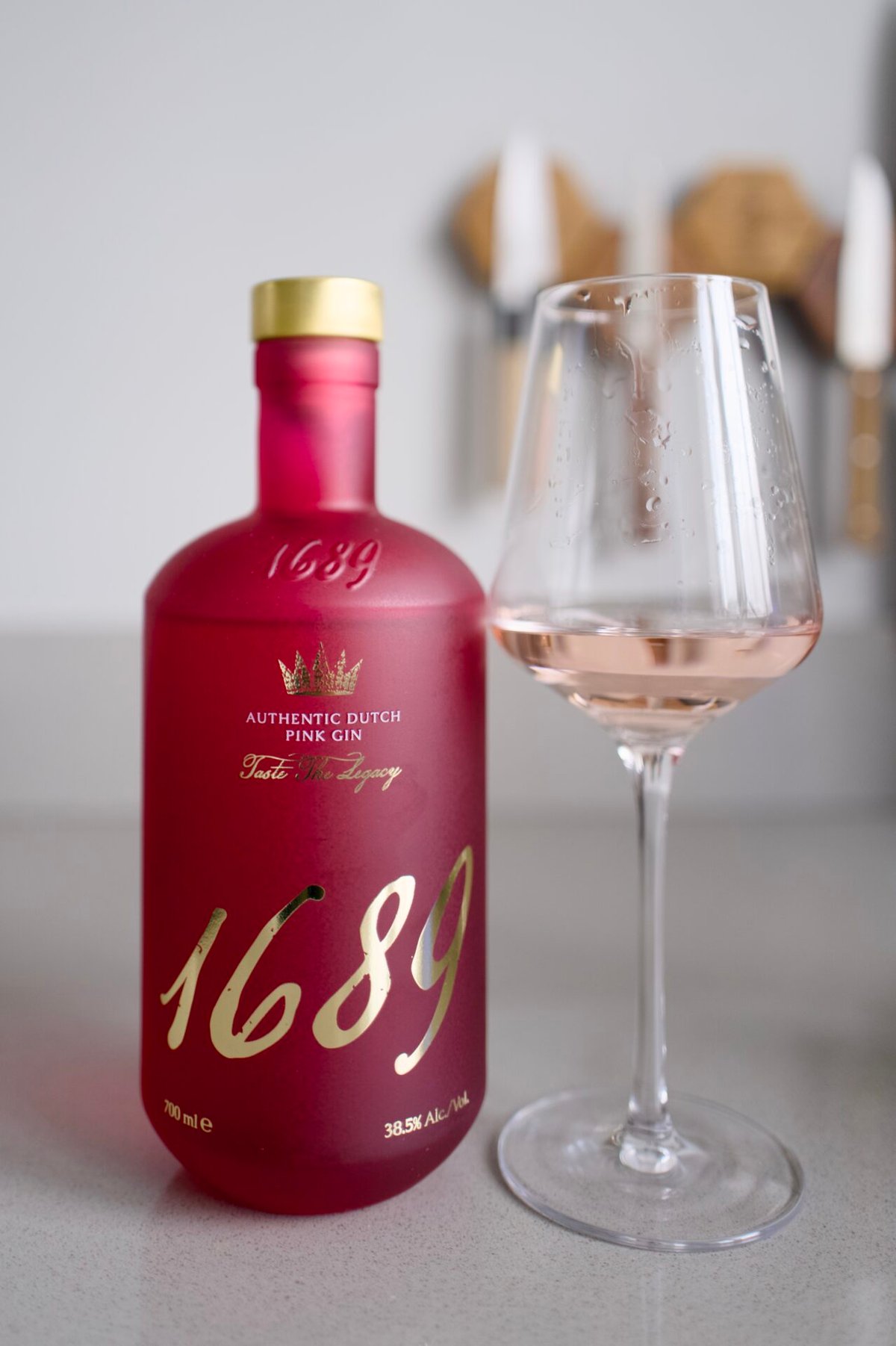 Pink frosted Gin 1689 Dutch Pink bottle with gold cap beside a glass of pale rosé gin