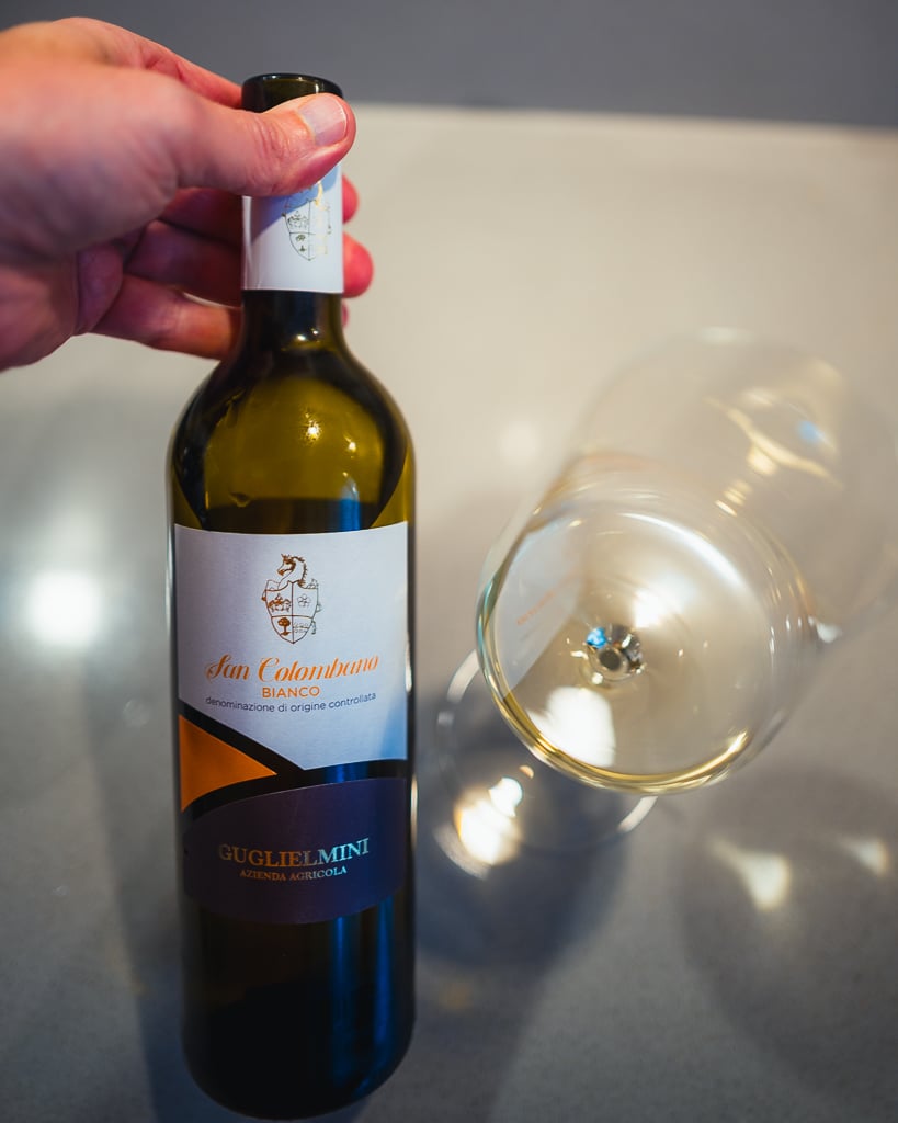 Hand holding the Guglielmini San Colombano Bianco bottle beside a glass of white wine