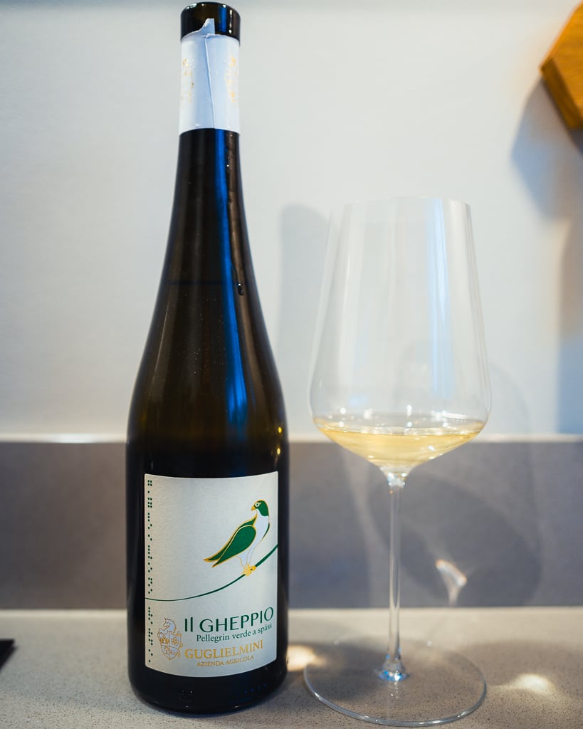 Guglielmini Il Gheppio white bottle with a green kestrel illustration beside a glass of white wine