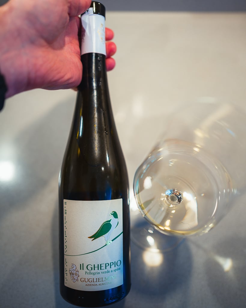 Hand holding the Guglielmini Il Gheppio bottle with green kestrel label beside a glass of white wine