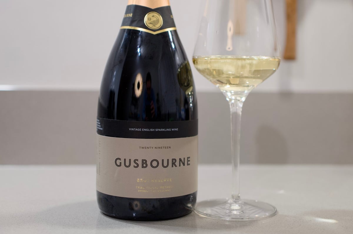 Gusbourne Brut Reserve bottle with gold foil neck beside a glass of sparkling wine