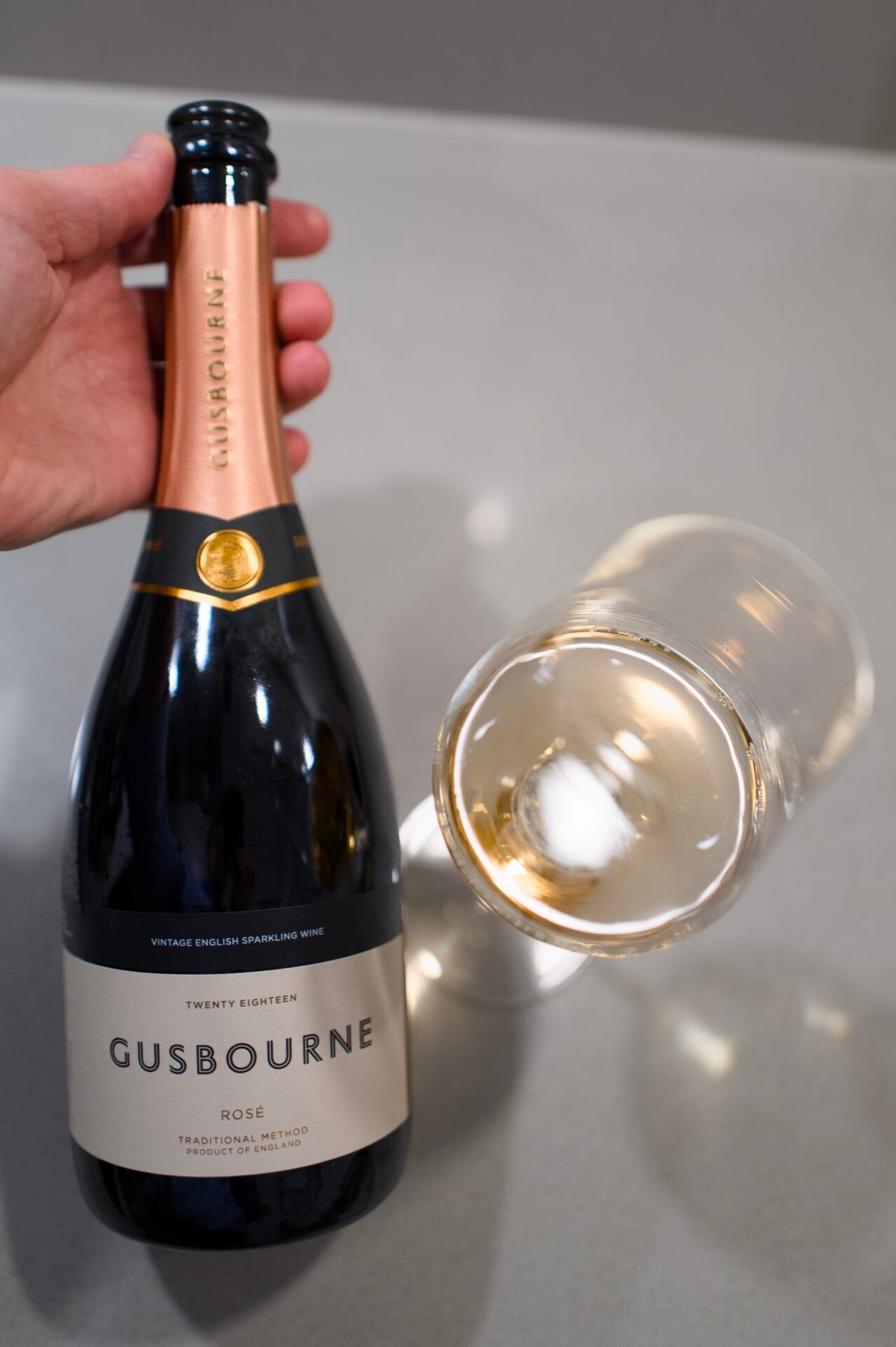 Hand holding a Gusbourne Rosé bottle next to a glass of salmon-pink sparkling wine