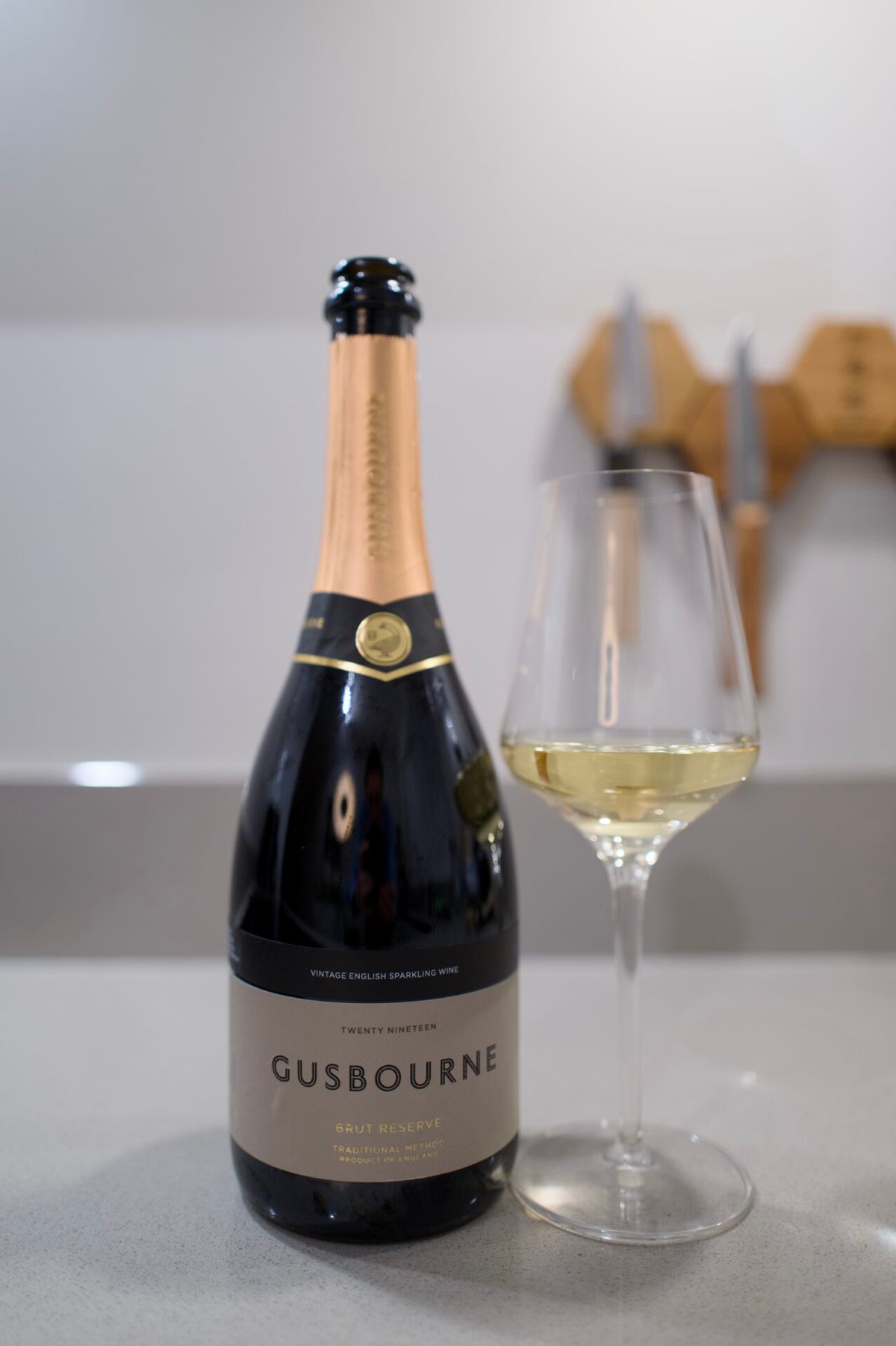Gusbourne Brut Reserve bottle with gold foil next to a glass of sparkling wine