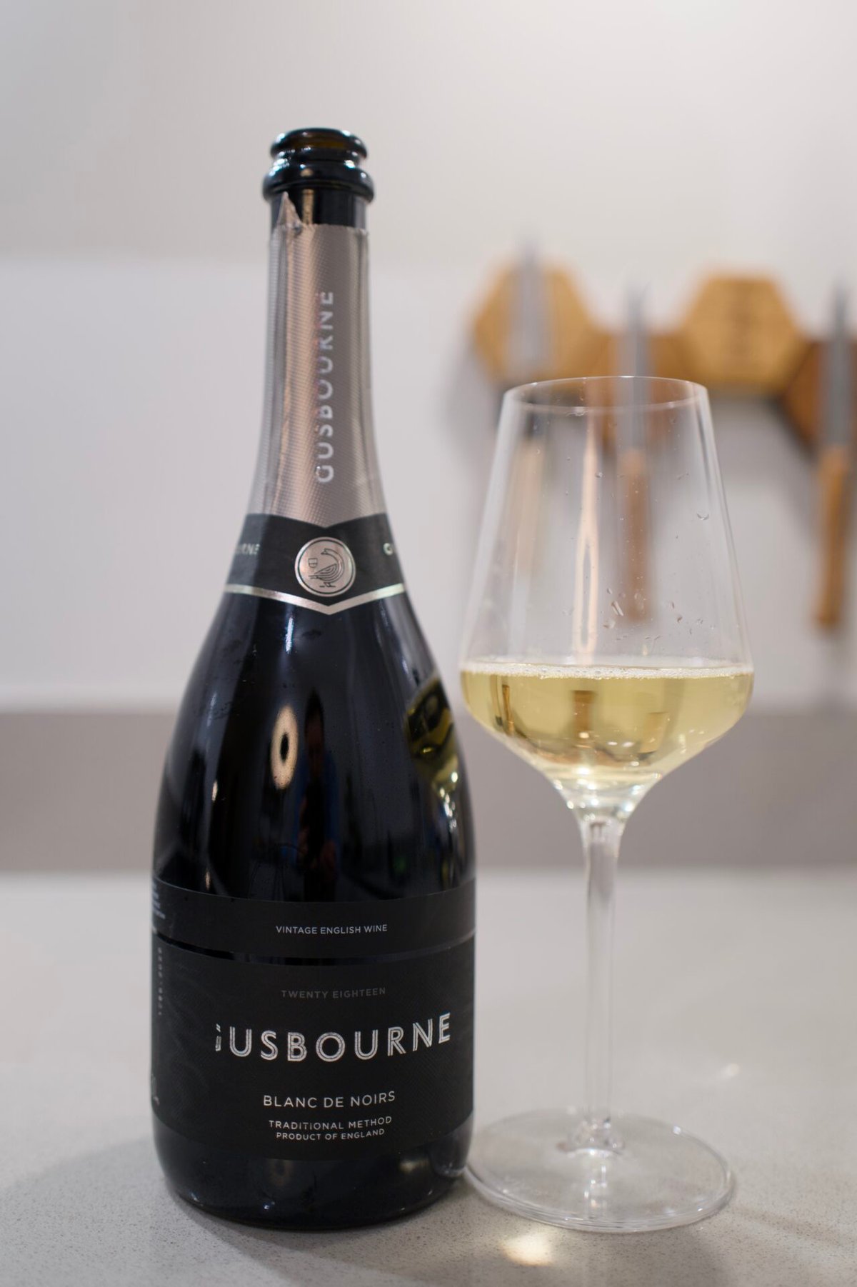 Gusbourne Blanc de Blancs bottle beside a glass of pale sparkling wine